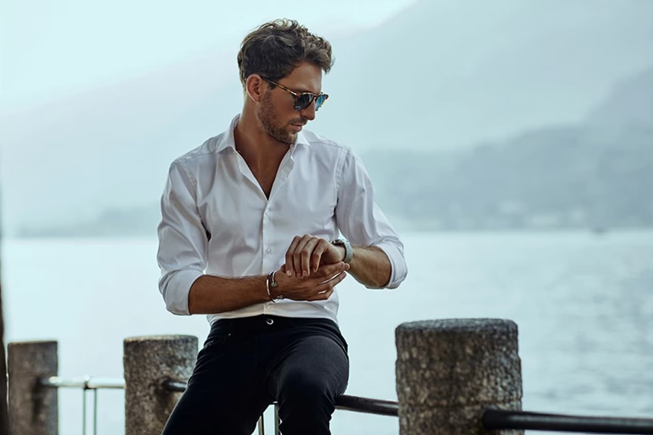 Man sitting on a dock, admiring his watch with the vast sea in the background—timeless style meets adventure.